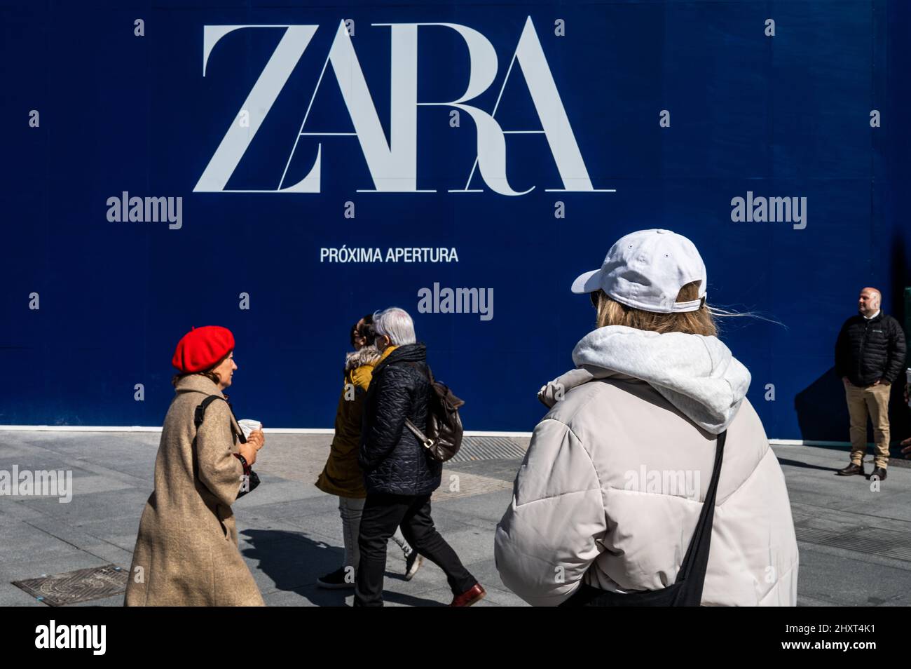 People walk past an advertisement for an upcoming opening of a Zara store. Zara shops are part of Inditex group, owned by Amancio Ortega. Stock Photo