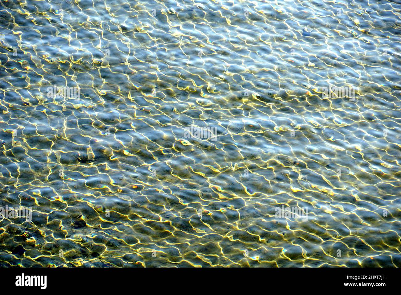 Interesting turquoise sea surface with yellow marbled sun reflection above transparent water Stock Photo