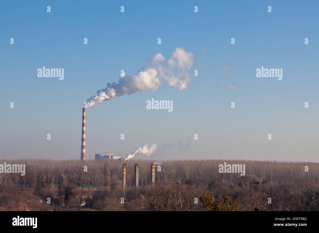 Smoke from a high smokestack against blue sky.  Chimney smoke from factory or a heating plants supplying heat to the city. Stock Photo