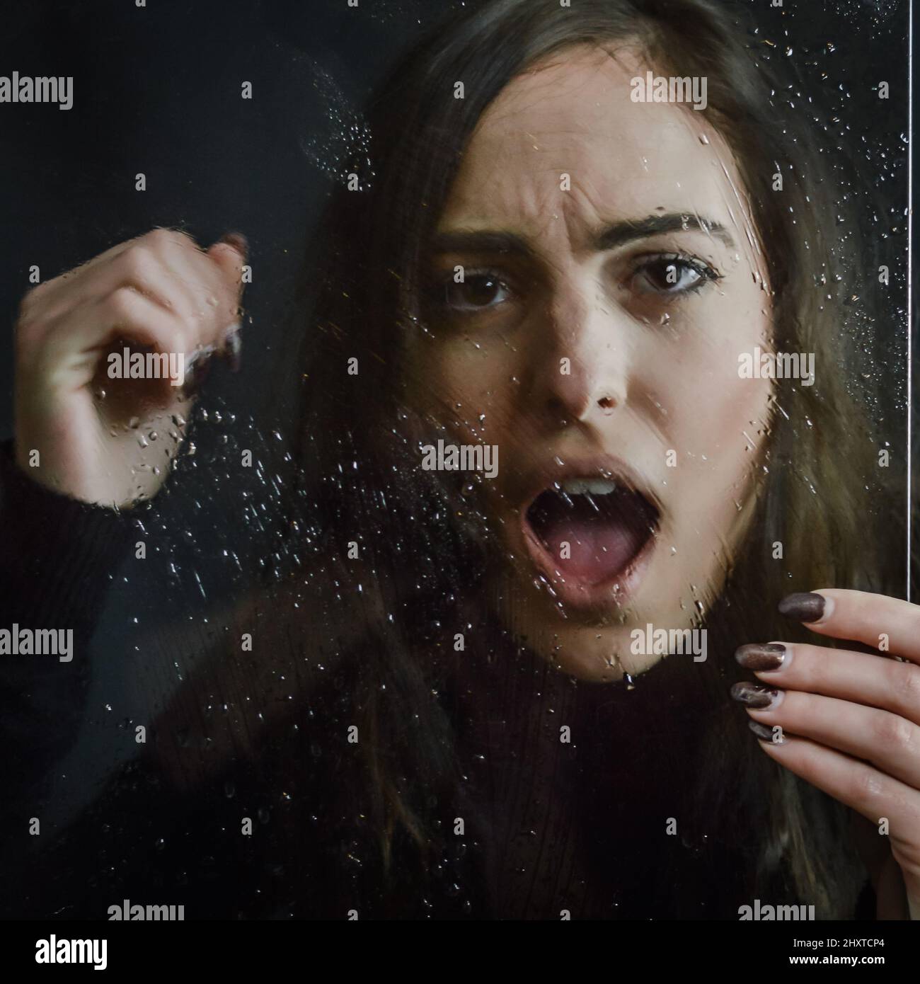 Portrait Of A Beautiful Girl Screaming And Placing Her Fist On A Wet Glass That She Holds