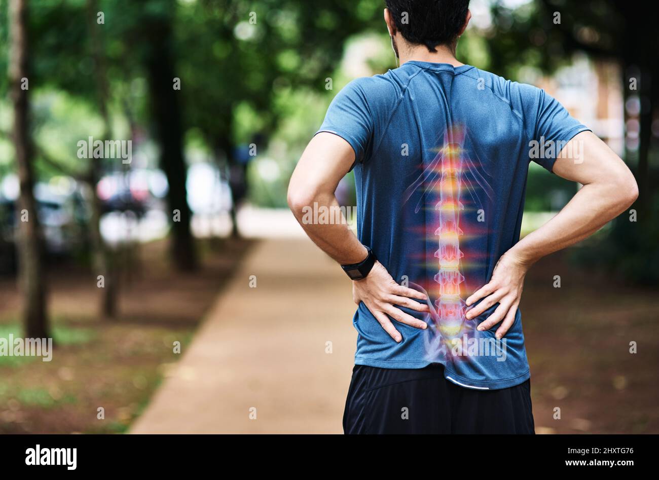 Hes overdone it this time with his training. Rear view shot of a sporty young man holding his back in pain while exercising outdoors. Stock Photo
