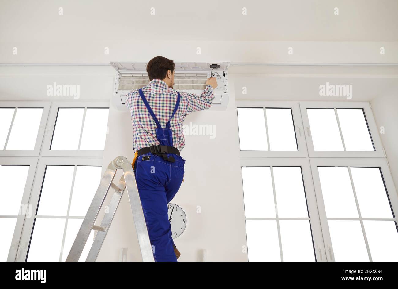 Repairman stand on ladder fix air conditioner Stock Photo