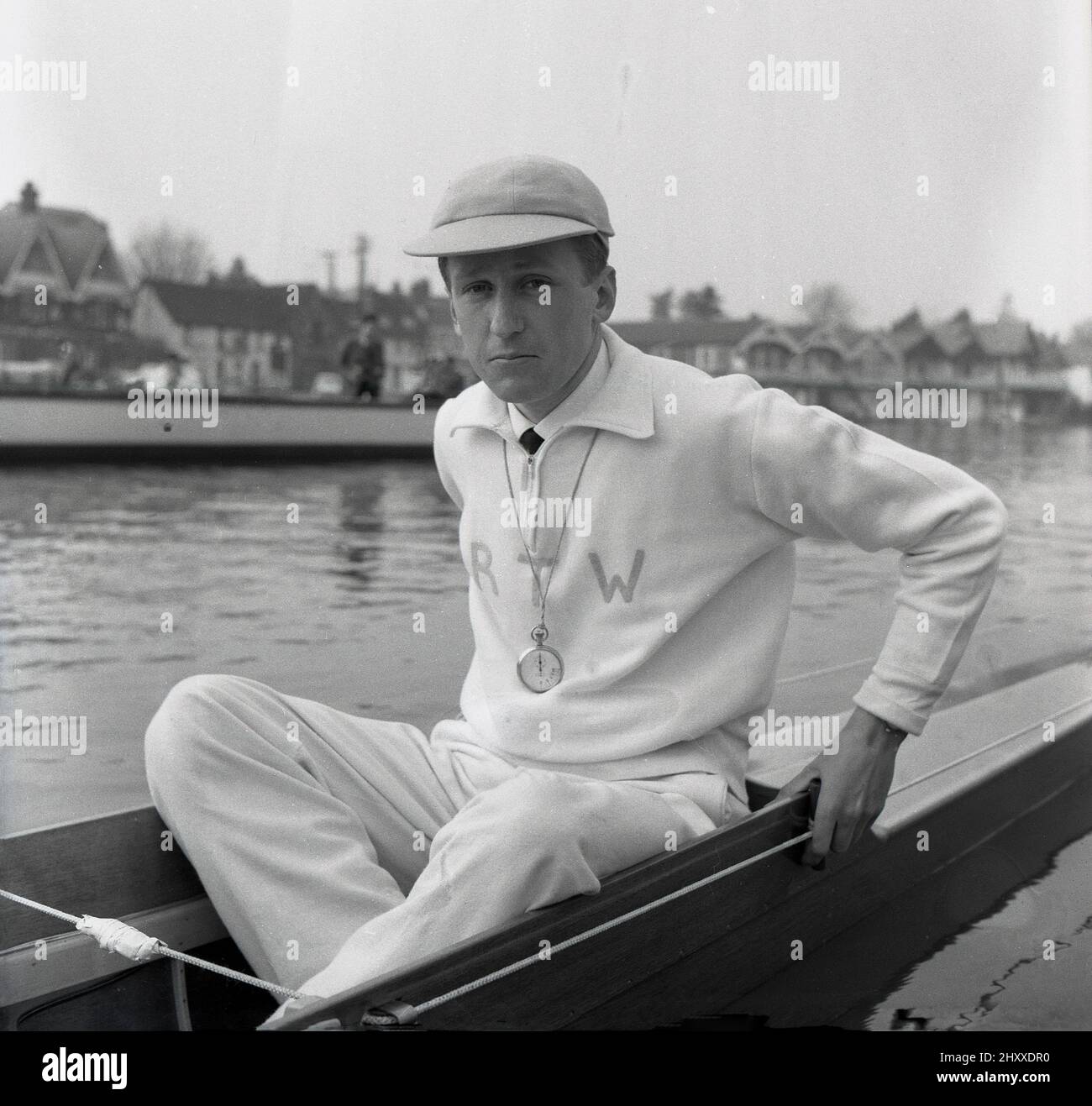 1961, historical, sitting in a rowing boat on the water, the coxswain or cox of the Cambridge University Boat team, R. T. Weston of Selwyn college, with cap and stopwatch. The initals RTW are embrodied on his cotton tracksuit top. Roger Weston had also been the Cambridge cox the previous year. The Oxford & Cambridge Boat Race, the famous university rowing race, first took place 1829 and is an annaul event on the River Thames over the championship course between Putney and Barnes in South West London. Stock Photo
