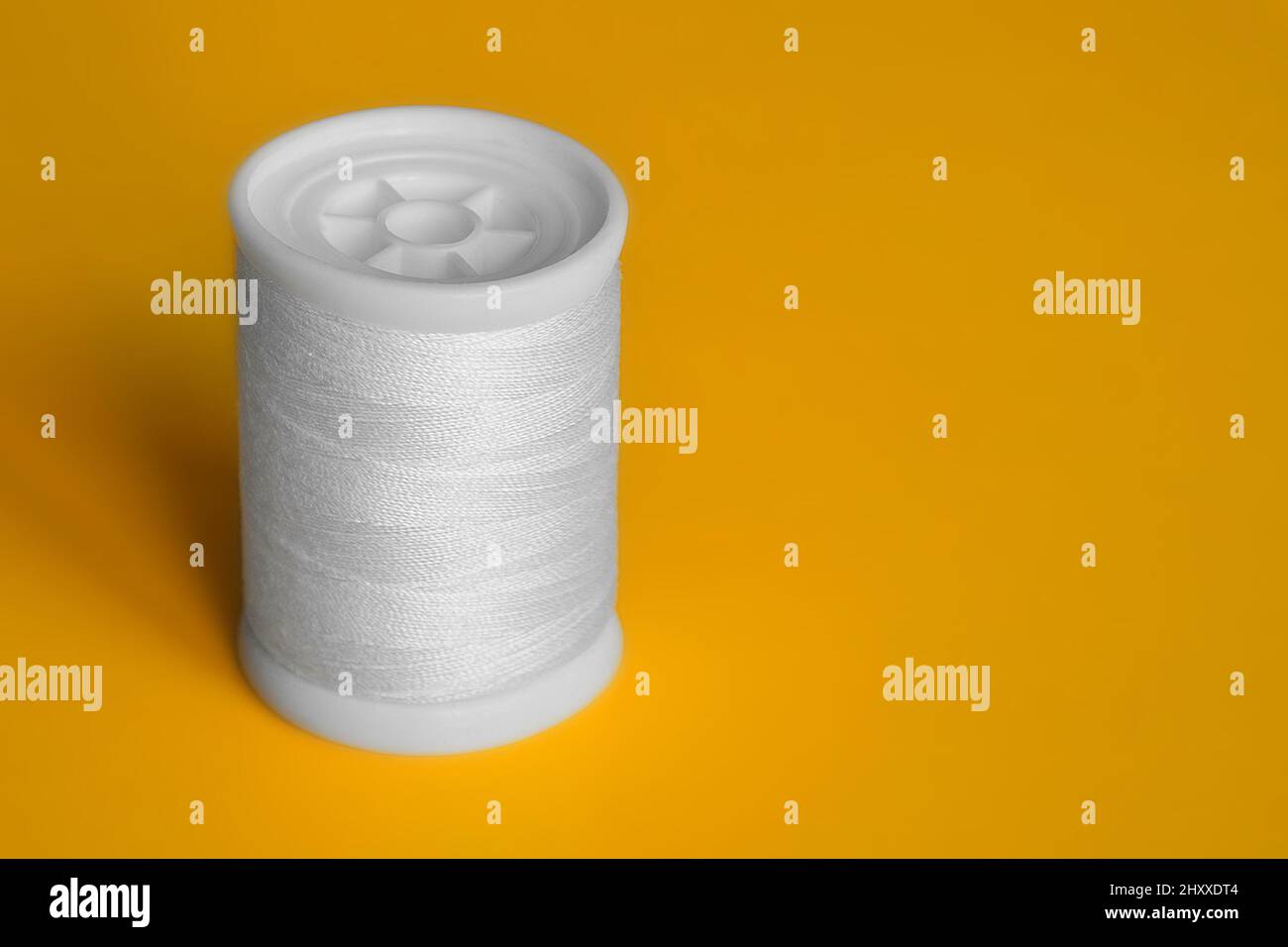 Reel of white sewing threads on yellow background. Copy space, close-up. Stock Photo