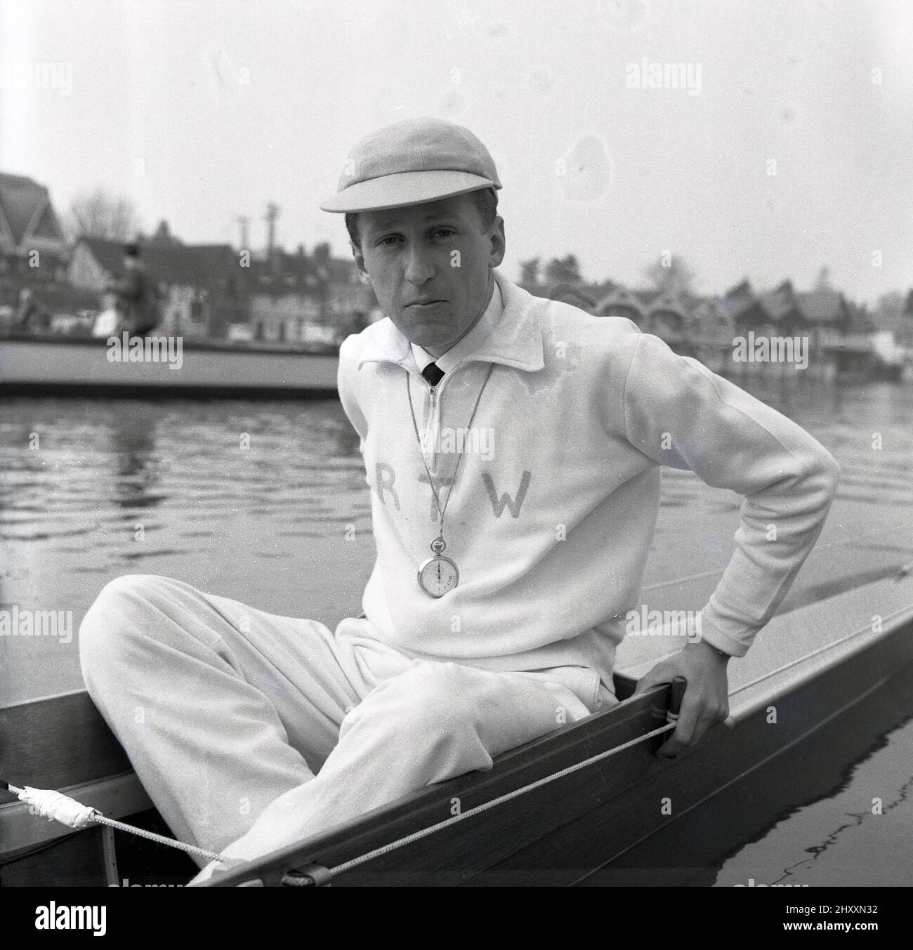 1961, historical, sitting in a rowing boat on the water, the coxswain or cox of the Cambridge University Boat team, R. T. Weston of Selwyn college, with cap and stopwatch. The initals RTW are embrodied on his cotton tracksuit top. Roger Weston had been the Cambridge cox the previous year. The Oxford & Cambridge Boat Race, the famous university rowing race, first took place 1829 and is an annaul event on the River Thames over the championship course between Putney and Barnes in South West London. Stock Photo