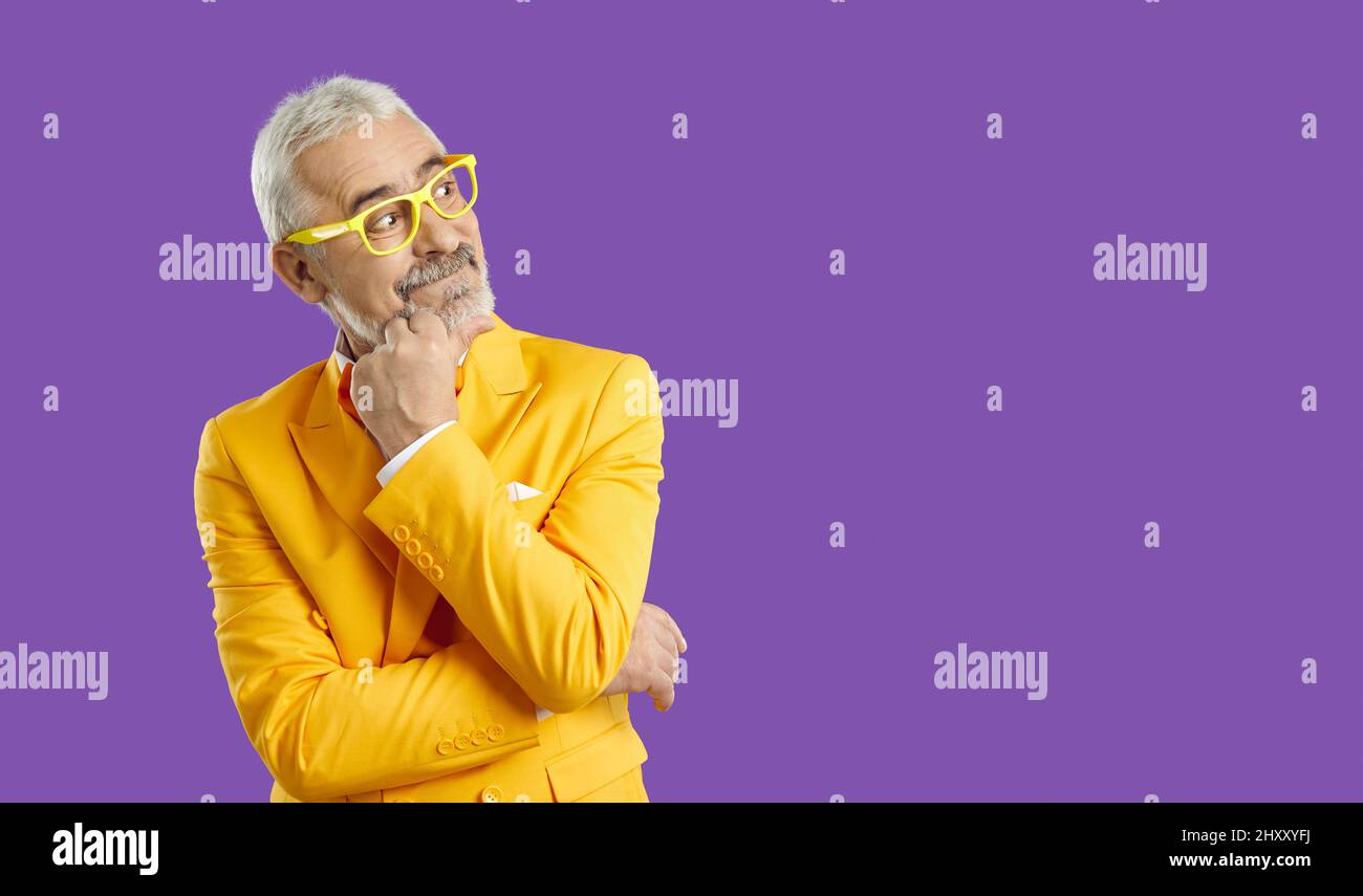 Funny happy senior man in yellow suit looking at purple copy space background and thinking Stock Photo