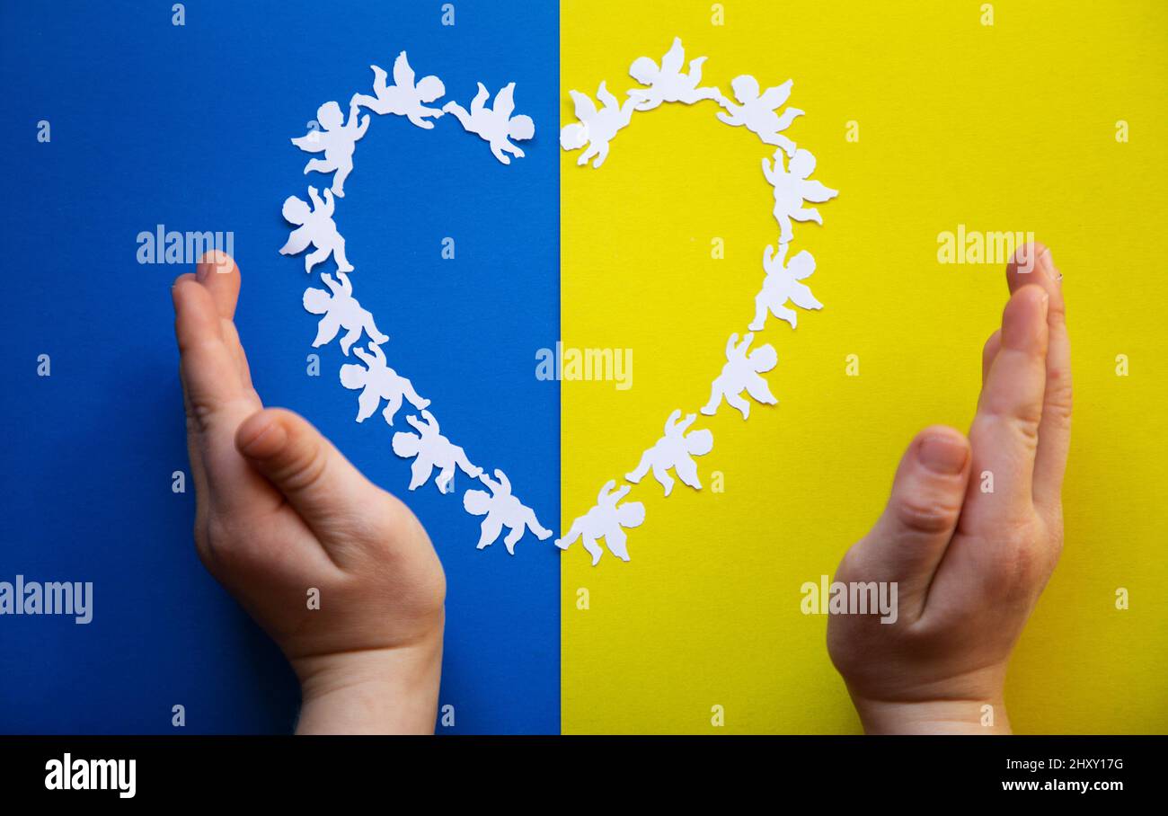 Heart, laid out of paper angels on yellow blue background in colors of Ukrainian flag, children's hands. children of Ukraine are against war, Ukrainia Stock Photo