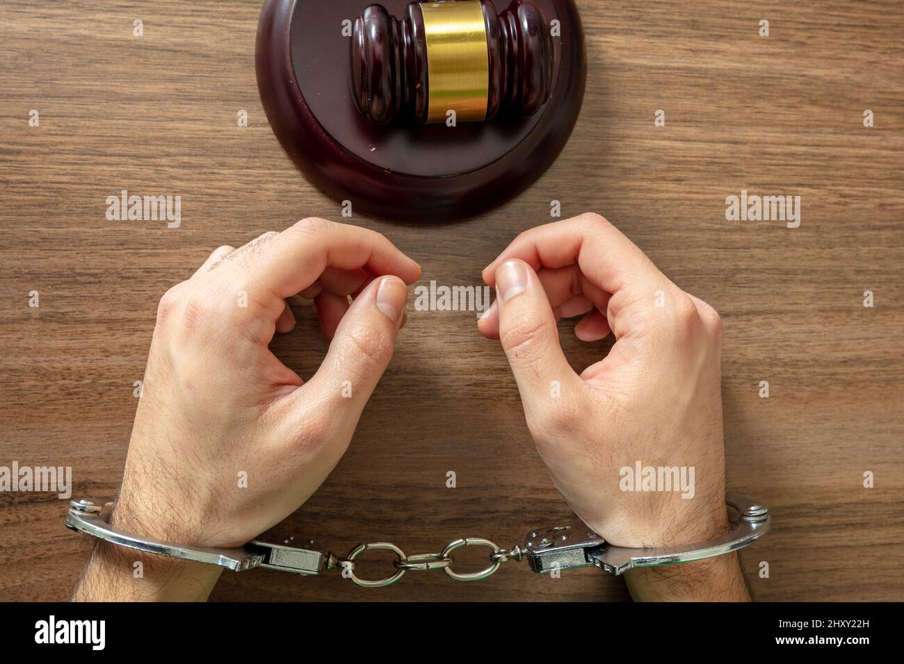 Law offender and Justice. Court sentence Prison. Handcuffed Convict, Handcuff locked and judge gavel on a wooden table, top view. Stock Photo