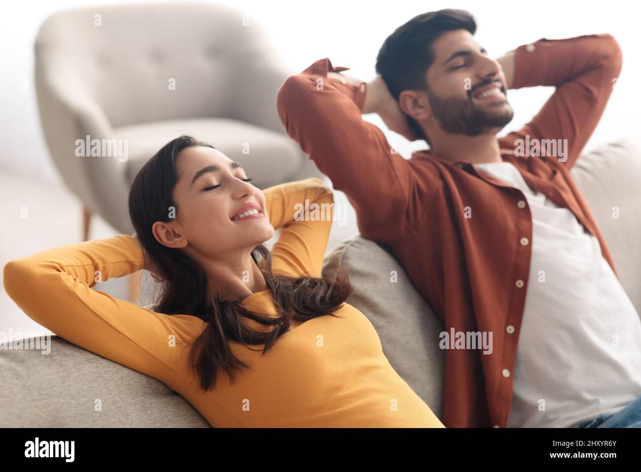 Relaxed Middle Eastern Spouses Sitting On Sofa Relaxing At Home Stock Photo