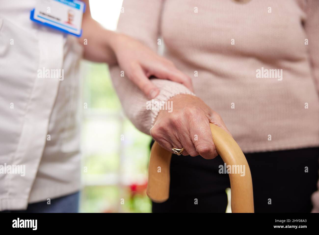 Close Up Of Senior Woman With Hands On Walking Stick Being Helped By Care Worker Stock Photo