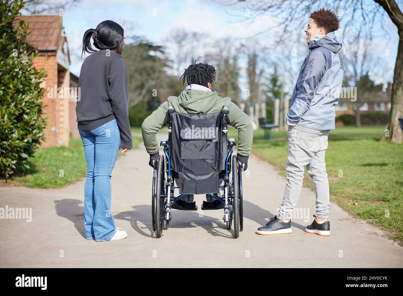 Teenage Boy In Wheelchair Hanging Out Talking And Laughing With Friends In Park Stock Photo