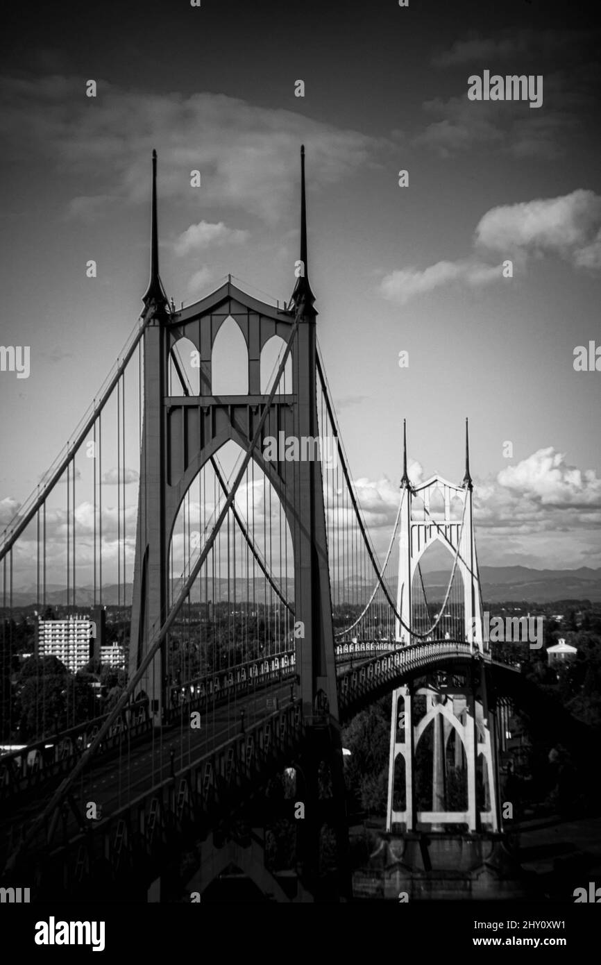 Vertical of a suspension bridge against a cityscape in grayscale Stock Photo