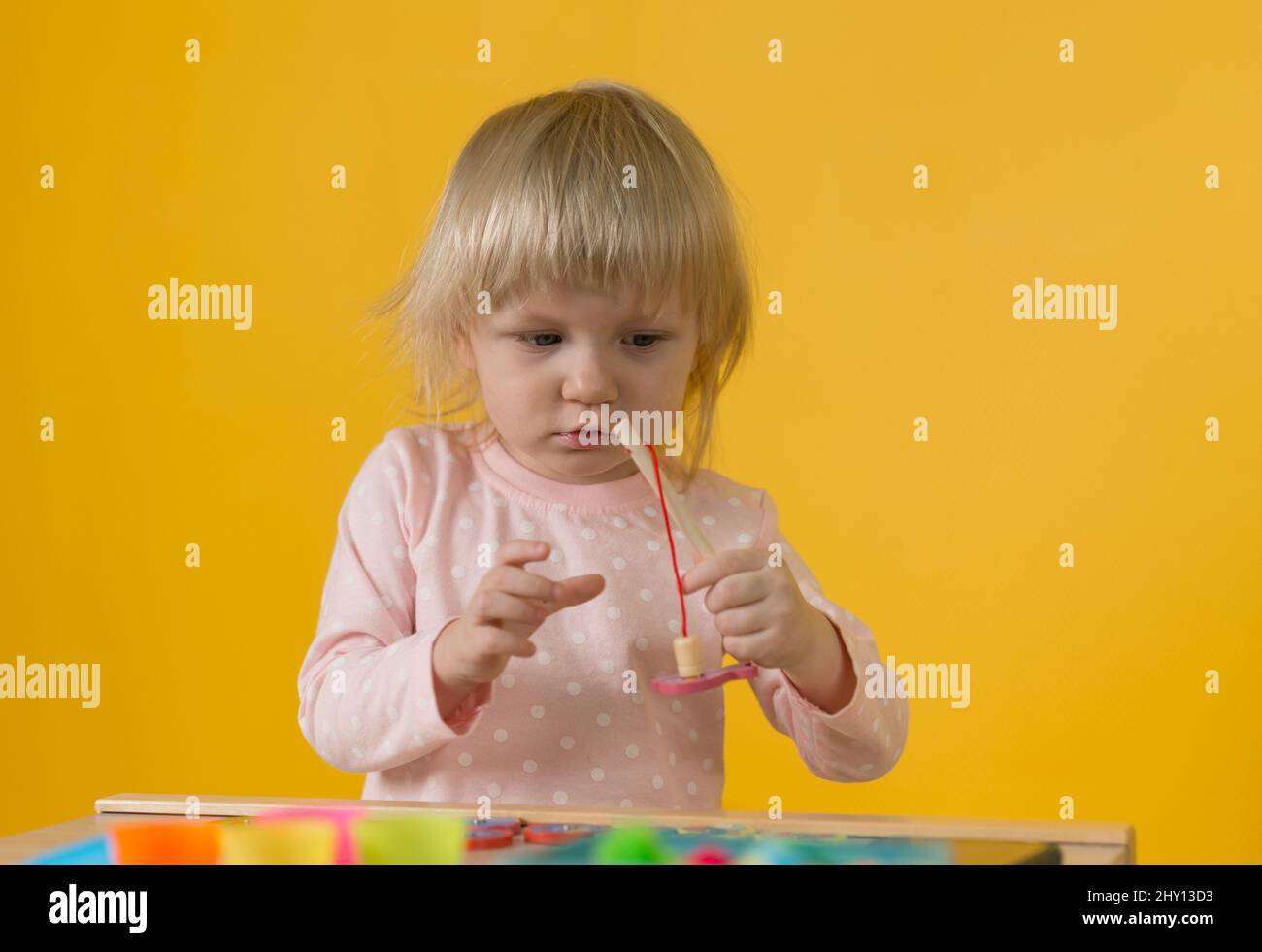 A girl in pink pajamas against a yellow wall enthusiastically plays a magnetic  fishing toy with a wooden fishing rod. Development of motor skills, att  Stock Photo - Alamy