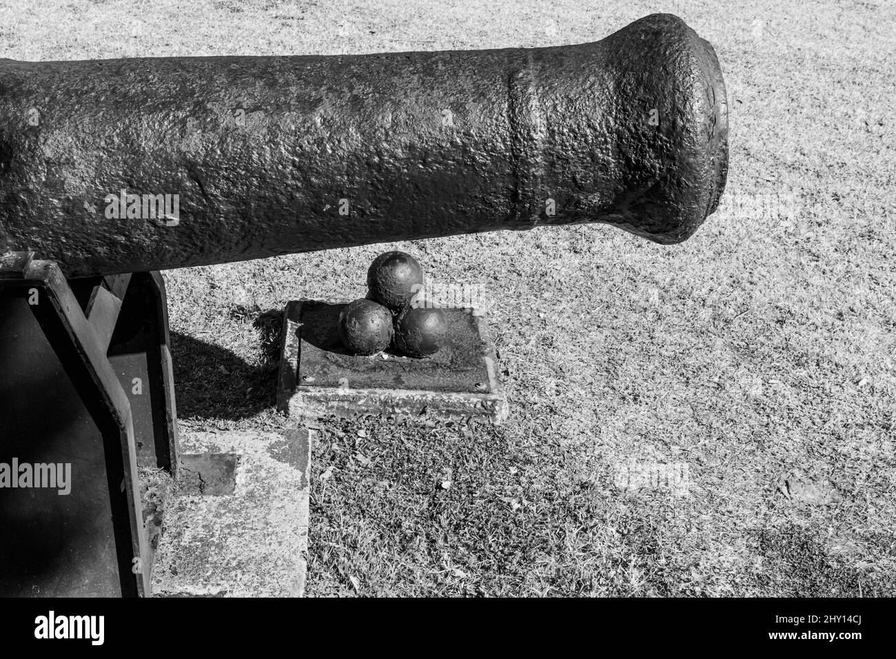 Grayscale shot of a vintage metal cannon with metal balls on the ground on a sunny day Stock Photo