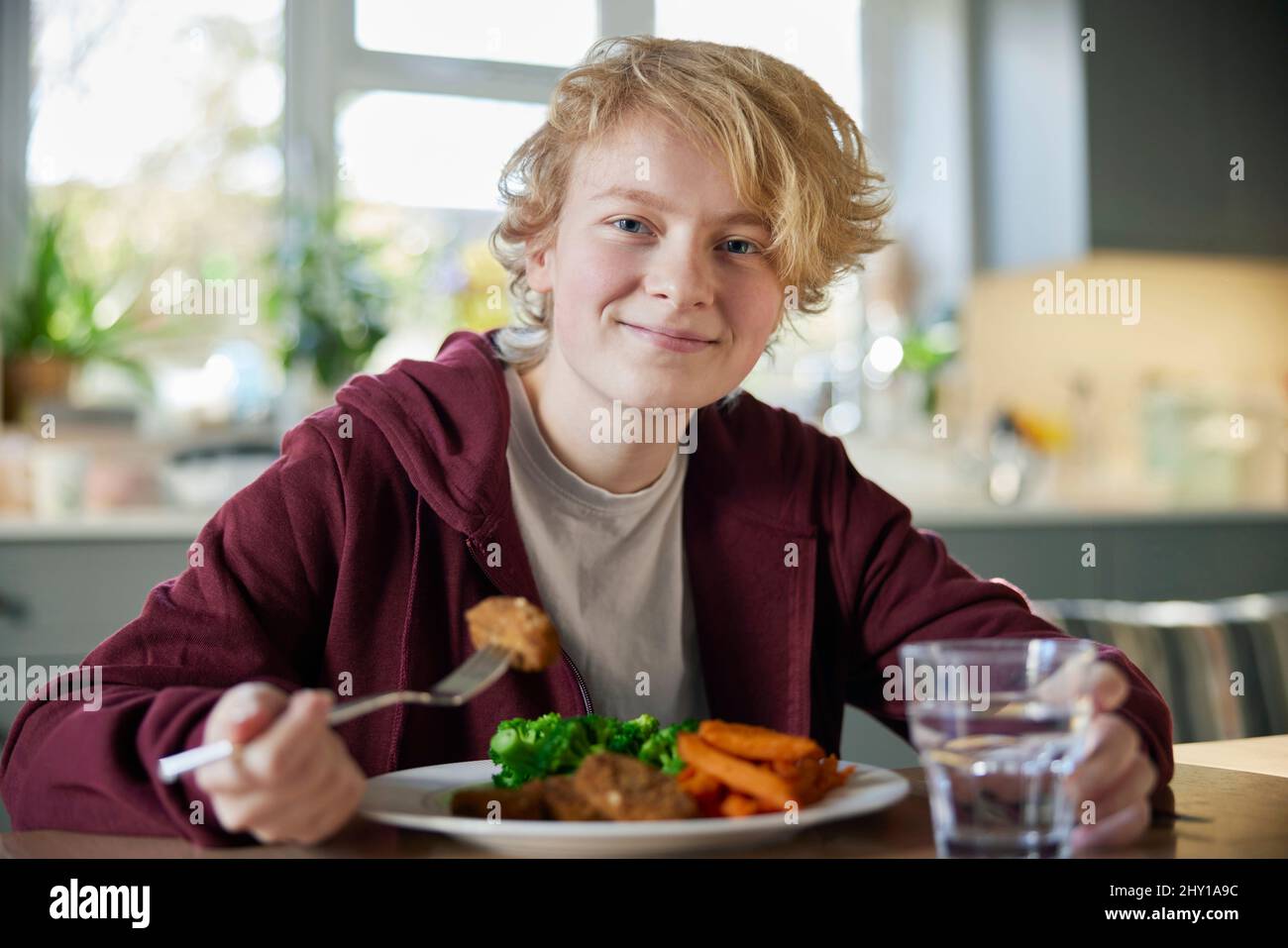 Portrait Of Teeange Girl Eating Vegan Meal Sitting At Table In Kitchen At Home Stock Photo