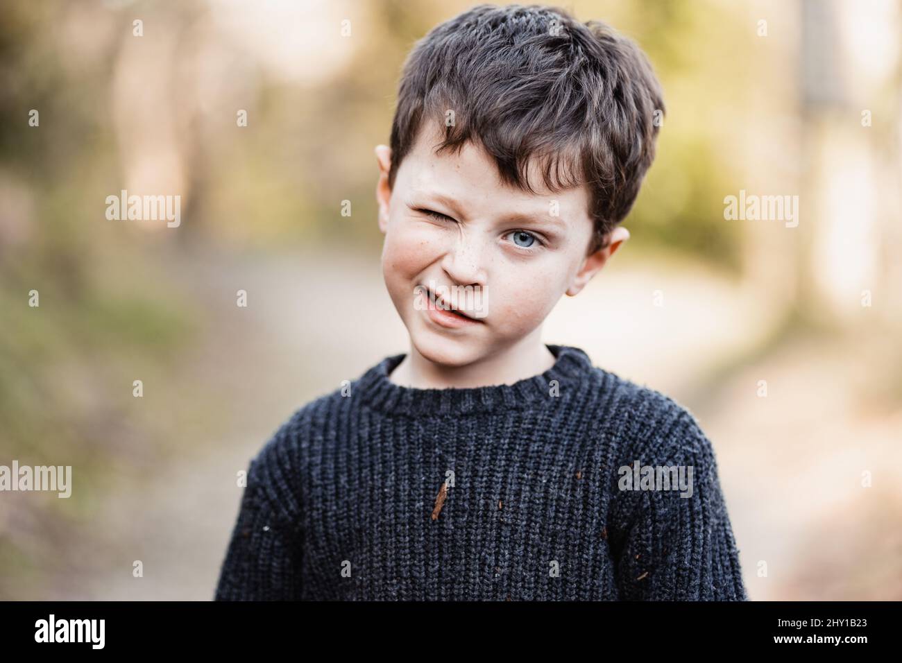 Cute little boy with blue eyes wearing warm sweater winking and looking at camera Stock Photo