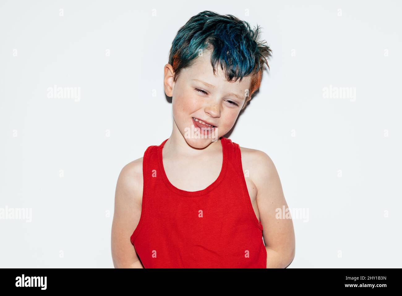 Mischievous boy with colorful dyed hair grinning and showing teeth while looking away on white background in light room Stock Photo