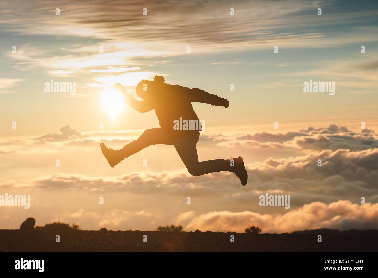 Full body side view of anonymous active tourist jumping on mountain above cloudy sky at sundown time during trip in highlands Stock Photo