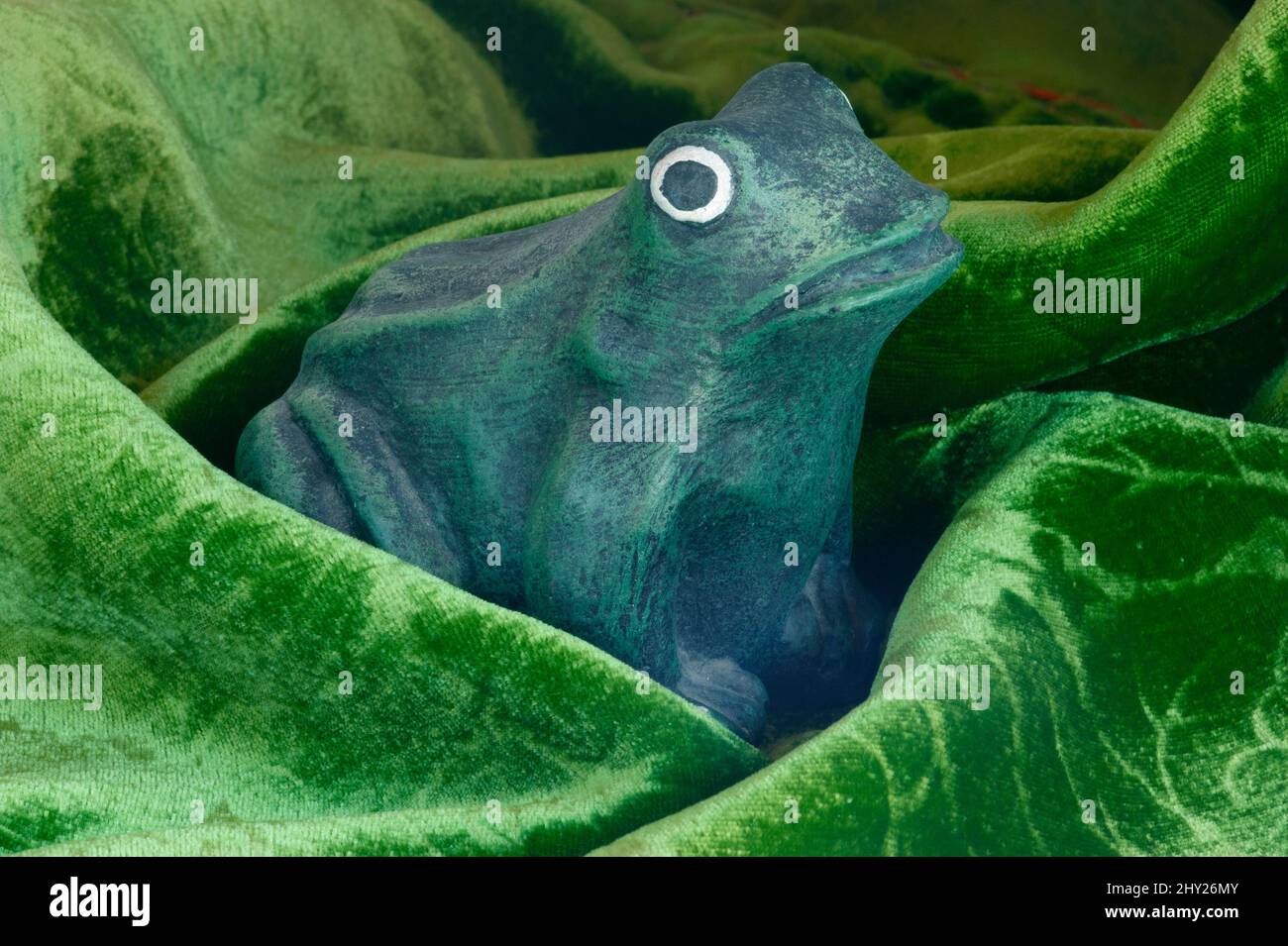 Green frog appears to be emerging from a bog. Storybook, fanciful figure using a cement frog & velvet fabric as the background. Frog has popping eyes. Stock Photo