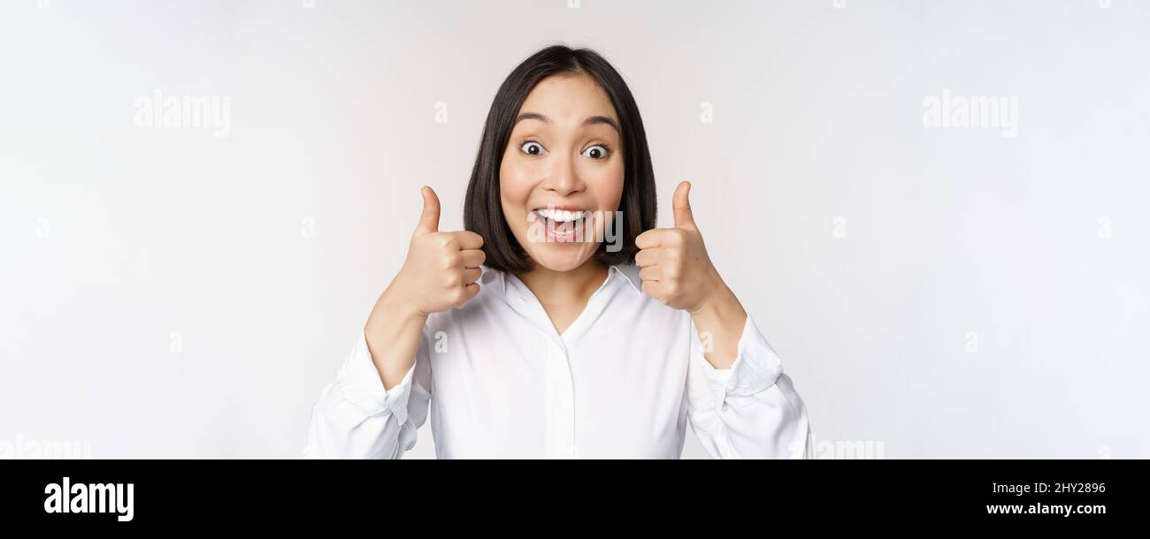 Enthusiastic asian girl showing thumbs up and smiling, pleased by ...