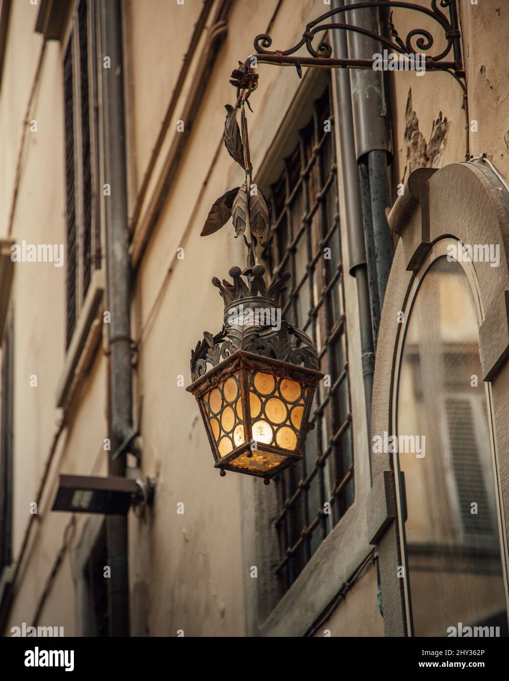 Vertical shot of a street lamp hanging from a metallic curved metal on the window. Stock Photo