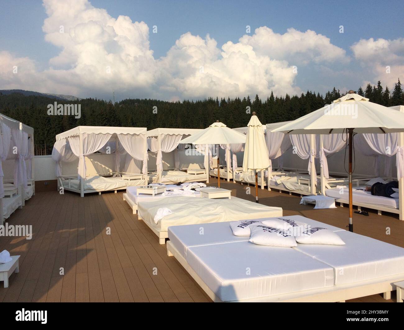 White canopy daybeds, parasols, and deck chairs in an enclosed area surrounded by dense forests Stock Photo