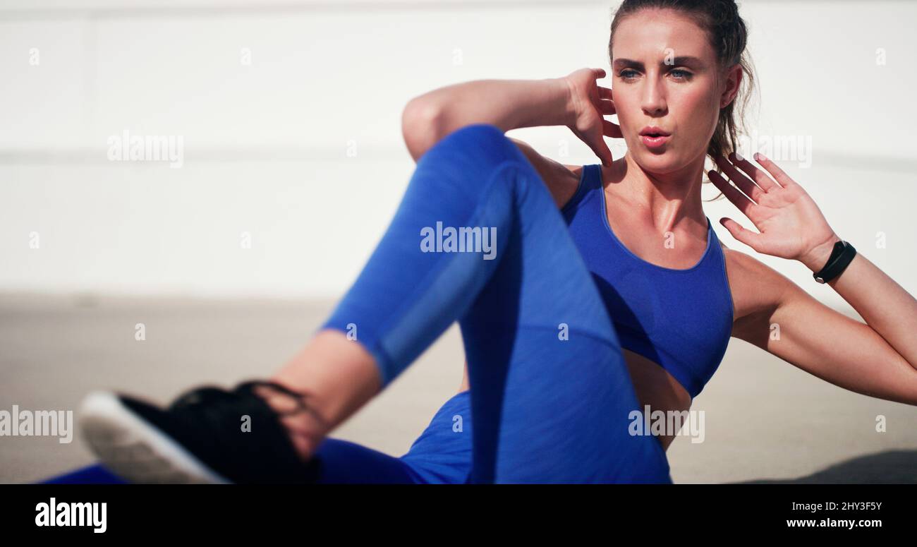 She wont stop till she reaches her target. Cropped shot of an attractive young sportswoman doing sit ups during a workout outdoors. Stock Photo