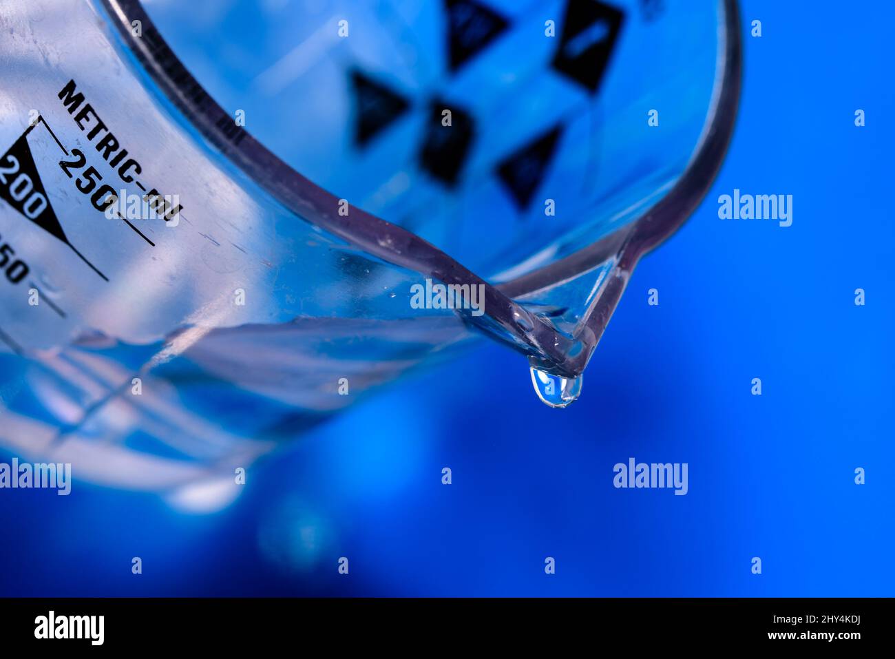 Macro shot of a water drop falling from a glass jug with blurred light