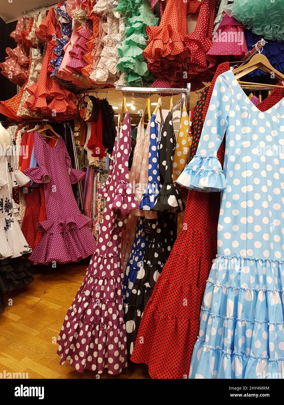 Flamenco dresses of various colors hanging on hangers in a store in
