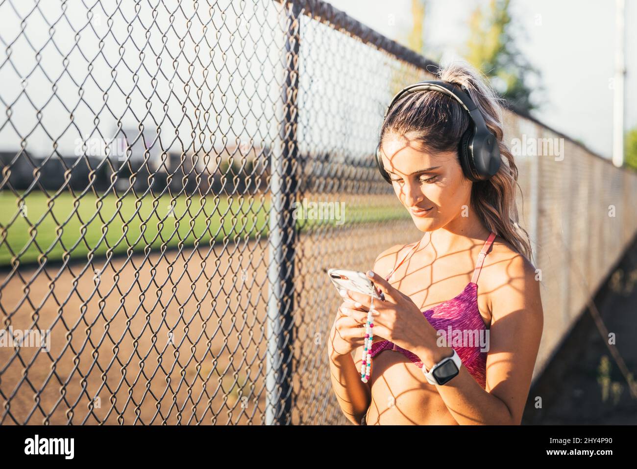 Young active woman using black wireless headphones and setting a music playlist on her smartphone before working out. Stock Photo