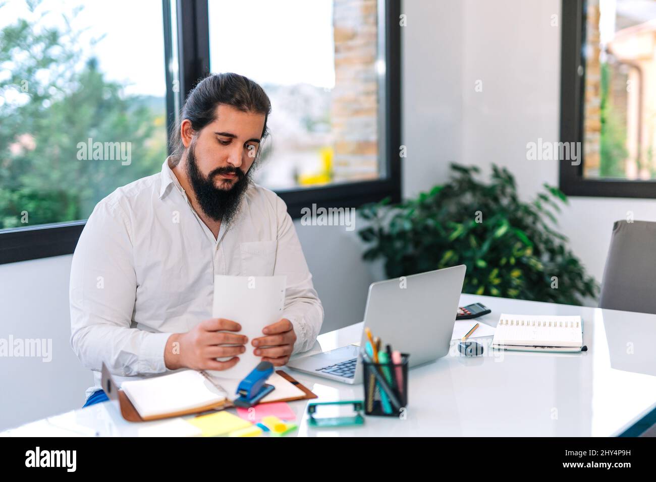 Young entrepreneur working on documents from home. Clear image of a young entrepreneur with a beard at work. Stock Photo