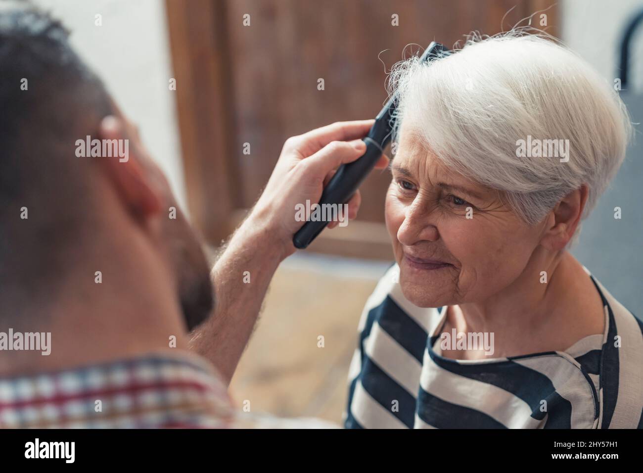 adult caucasian son taking care of his elderly mother by combing her short grey hair. High quality photo Stock Photo