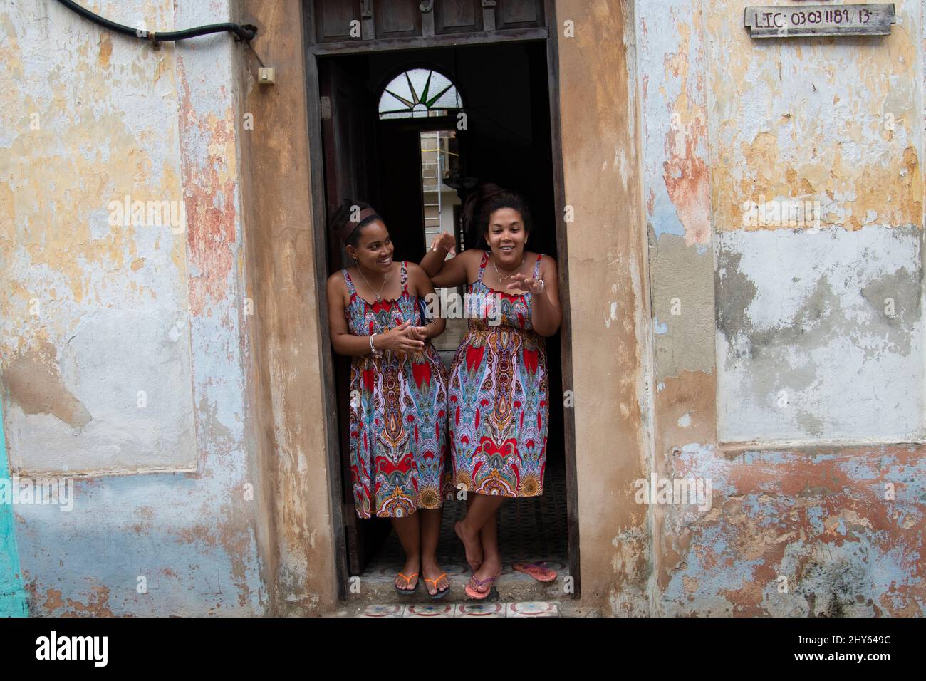 Two young Cuban female women dressed alike laugh in the doorway of their home in Havana, Cuba. Stock Photo