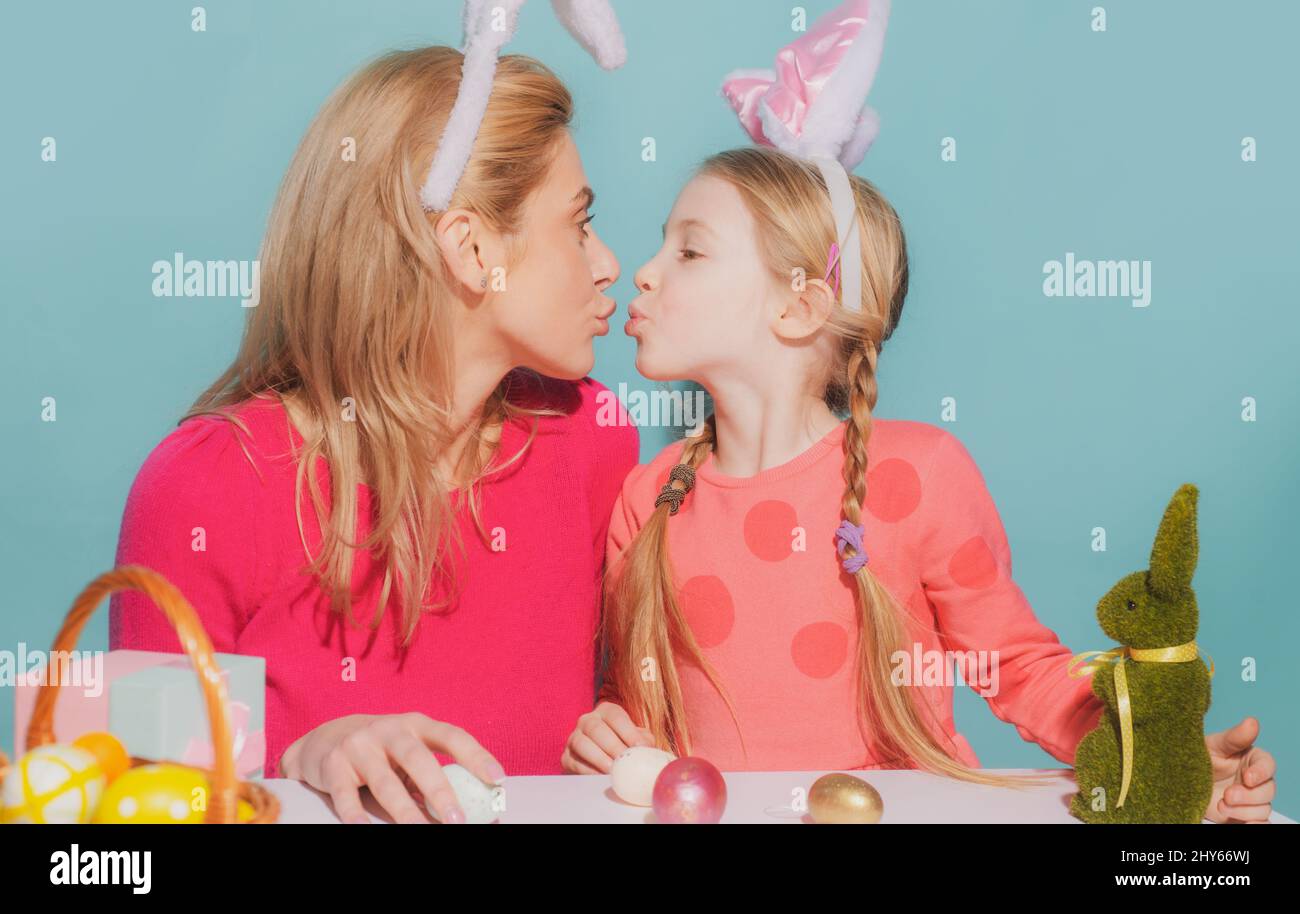 Mother and daughter preparing for Easter and kissing. Cute little child girl with mom wearing bunny ears on Easter day. Stock Photo