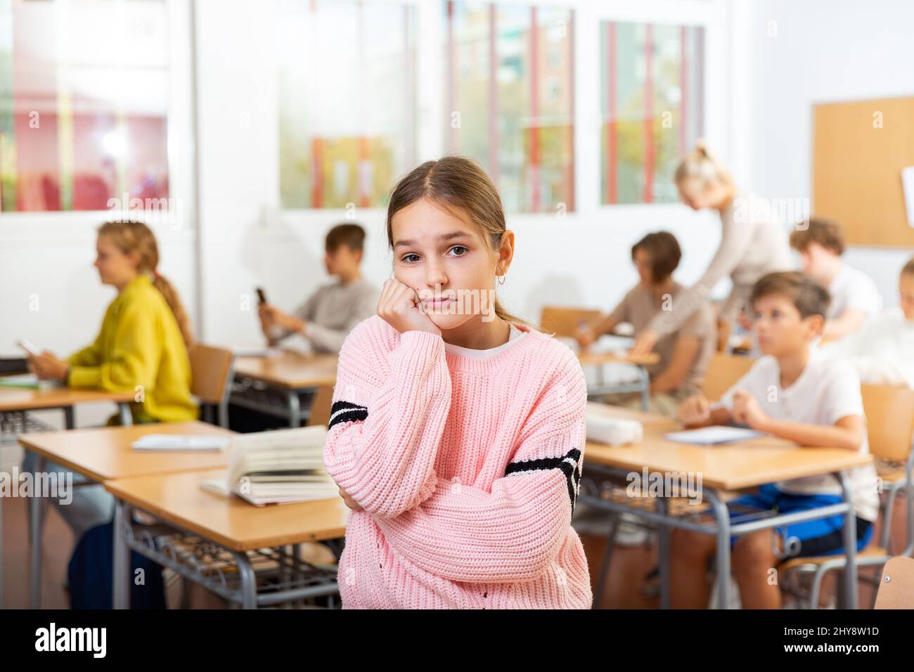 Upset girl stands in a school class against background of classmates ...