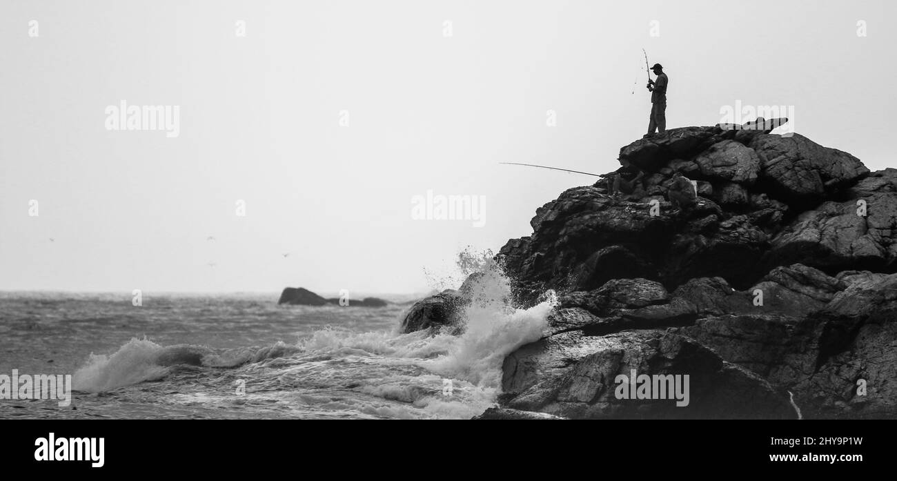 View of a fisherman standing on top of the rocks near the sea Stock Photo