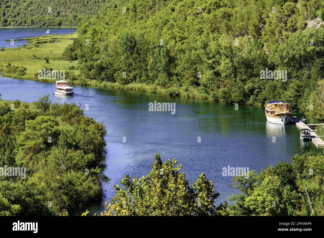 Aerial shot of a winding calm river with boats flowing through a forest in Krka National Park Stock Photo
