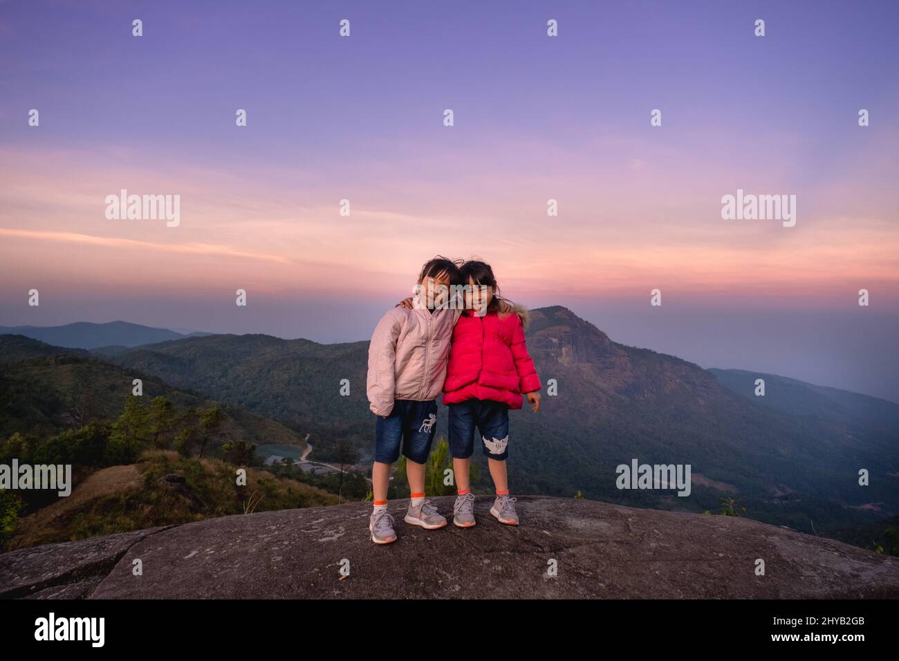Two cute little girls hugging on top of a mountain and looking at the ...