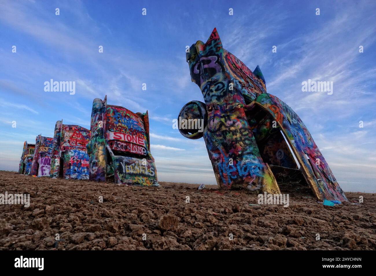 Cadillac Ranch is not a ranch but a public art installation and sculpture in Amarillo, Texas, USA. Used Cadillac automobiles are half-buried nose-first in the ground, at an angle corresponding to that of the Great Pyramid of Giza in Egypt, and show off the different styles of tail fins. Cadillac Ranch is visible from the highway, off Route 66. Located on private land, visiting is encouraged. In addition, writing graffiti on or spray-painting the vehicles is now encouraged. Everytime you visit, its is a different experience, for it is always changing Stock Photo