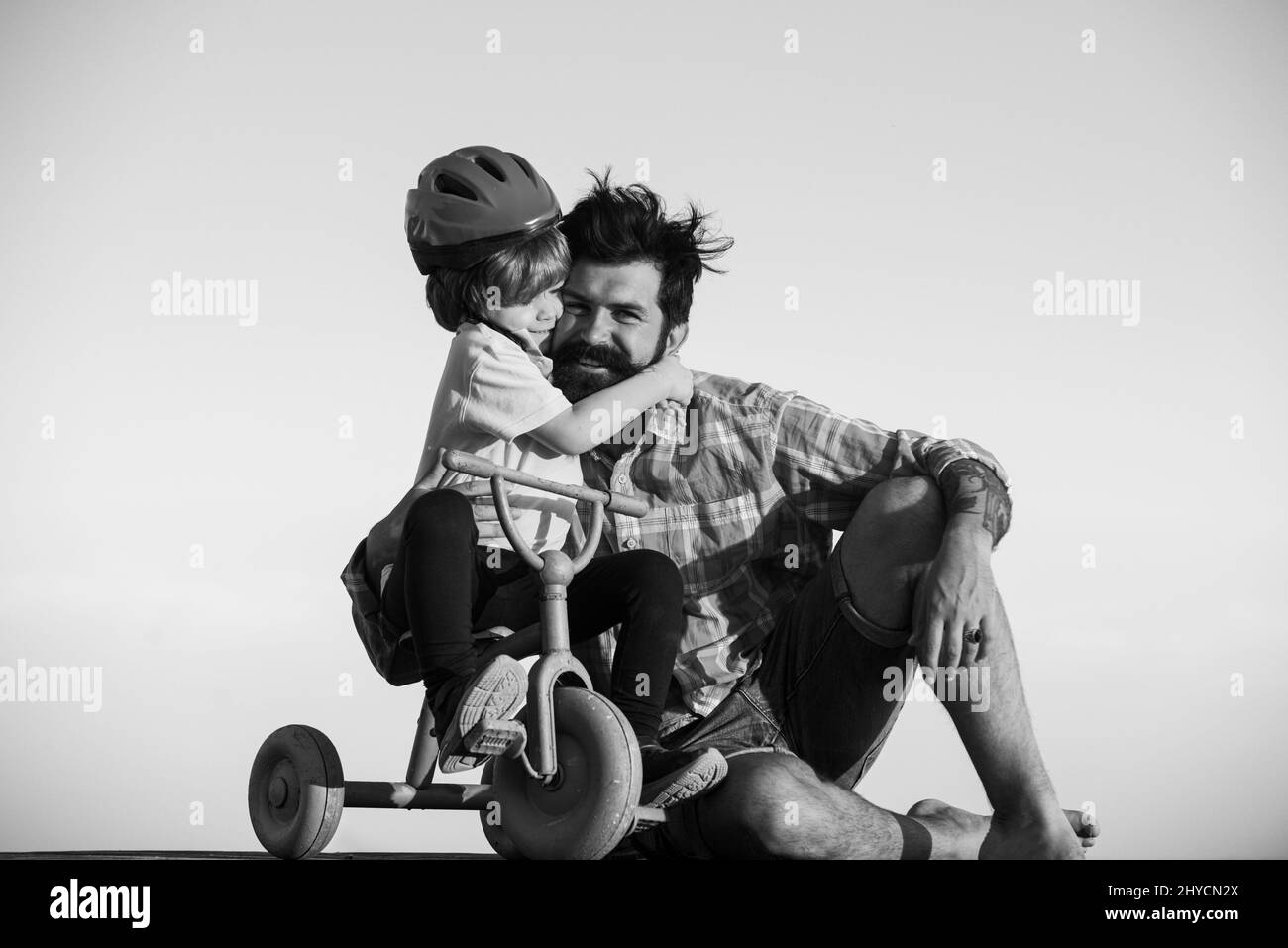 Lovely father teaching son riding bike. Happy dad helping excited son to ride a bicycle. Young smiling boy wearing helmet while learning to ride cycle Stock Photo