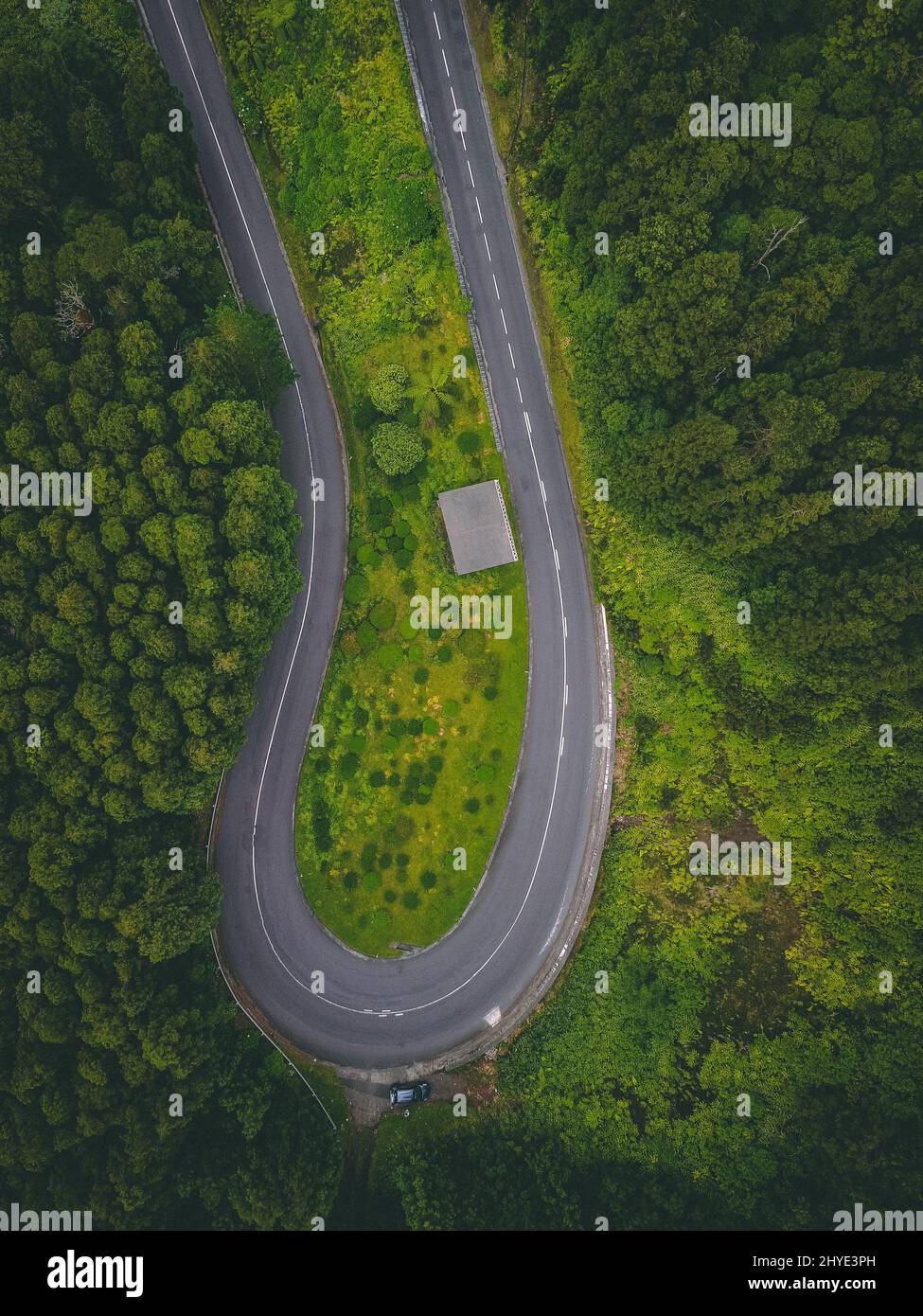 Aerial shot of a sharp rotation of the road surrounded by green fields ...