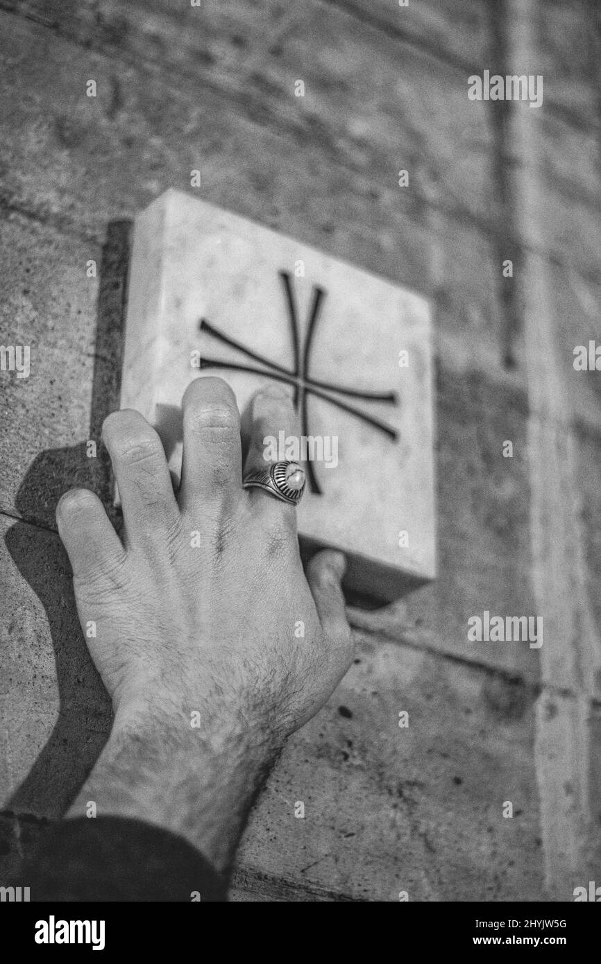 Vertical grayscale closeup of the man's hand touching the cross. Stock Photo