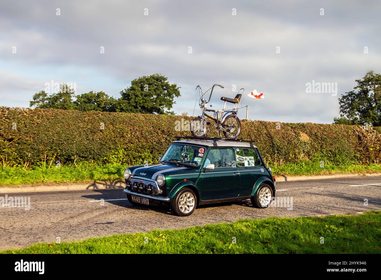 2000 green Rover Mini Cooper Sport with Chopper bicycle on roof rack flying Union Jack Flag; en-route to Capesthorne Hall classic August car show, Cheshire, UK Stock Photo