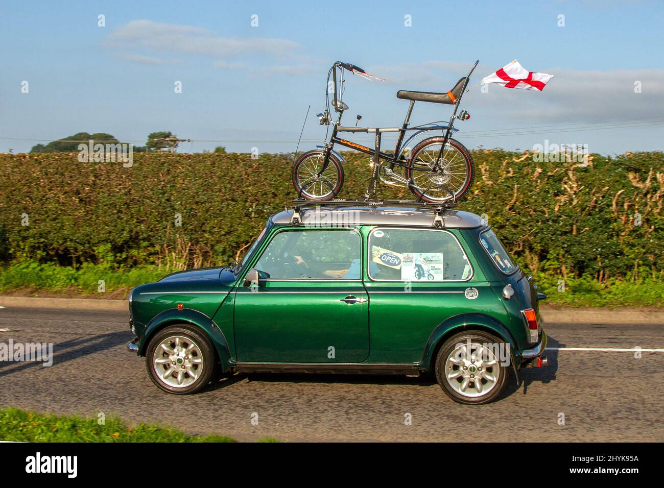2000 green Rover Mini Cooper Sport with Chopper bicycle on roof rack flying Union Jack Flag; en-route to Capesthorne Hall classic August car show, Cheshire, UK Stock Photo