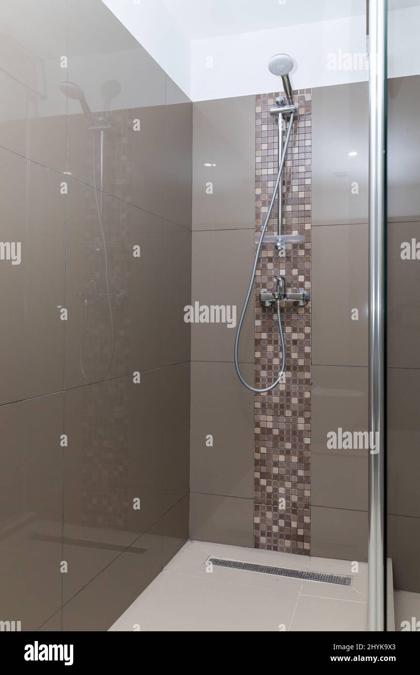 Modern design of the shower cabin with a piece of vertical mosaic on