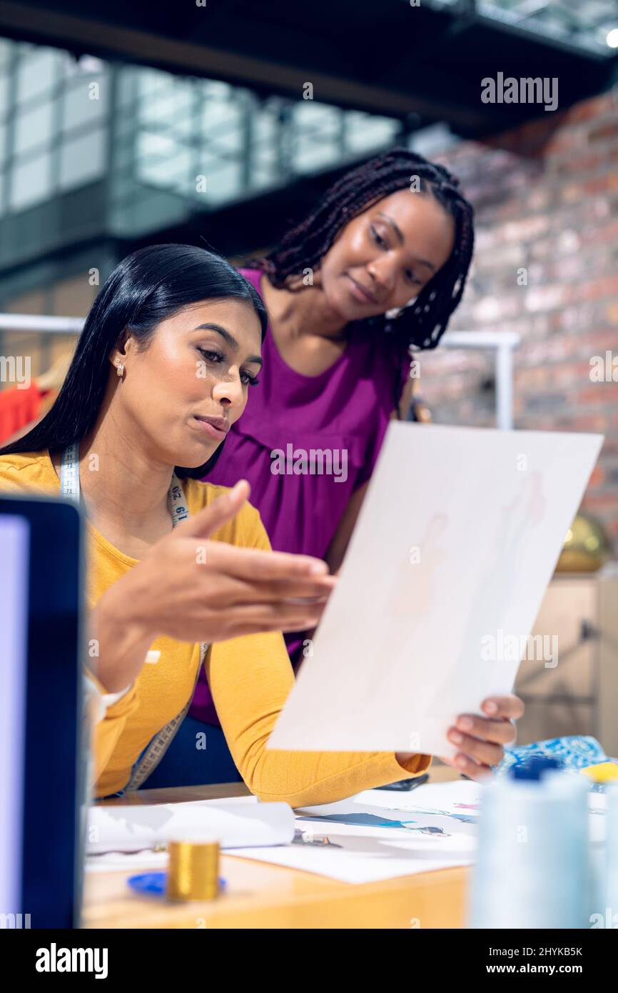 Multiracial young female fashion designers discussing over dress drawings at desk Stock Photo