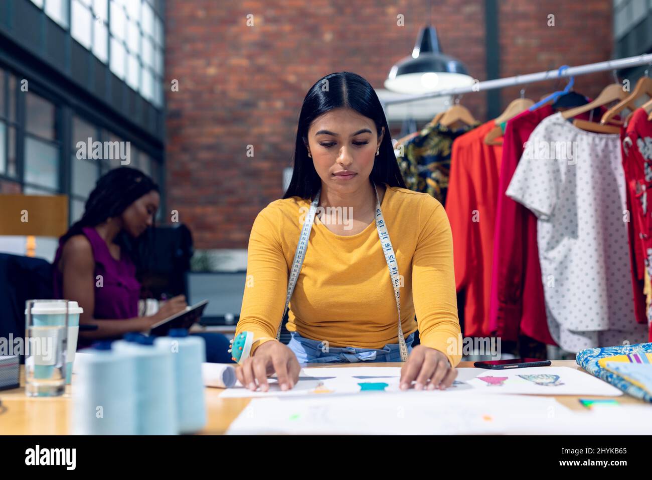 Biracial young female fashion designer working over dress drawings at desk Stock Photo