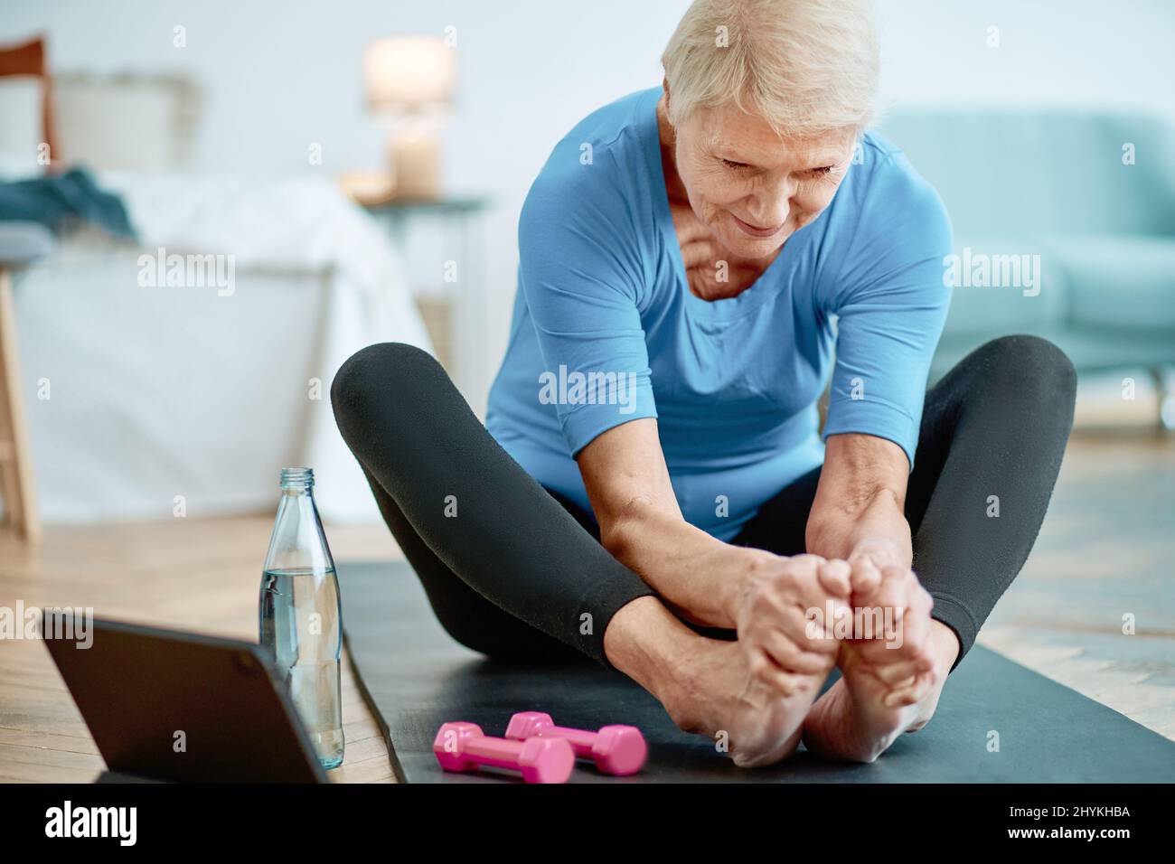 elderly woman sitting in a yoga pose in front of an open laptop Stock ...