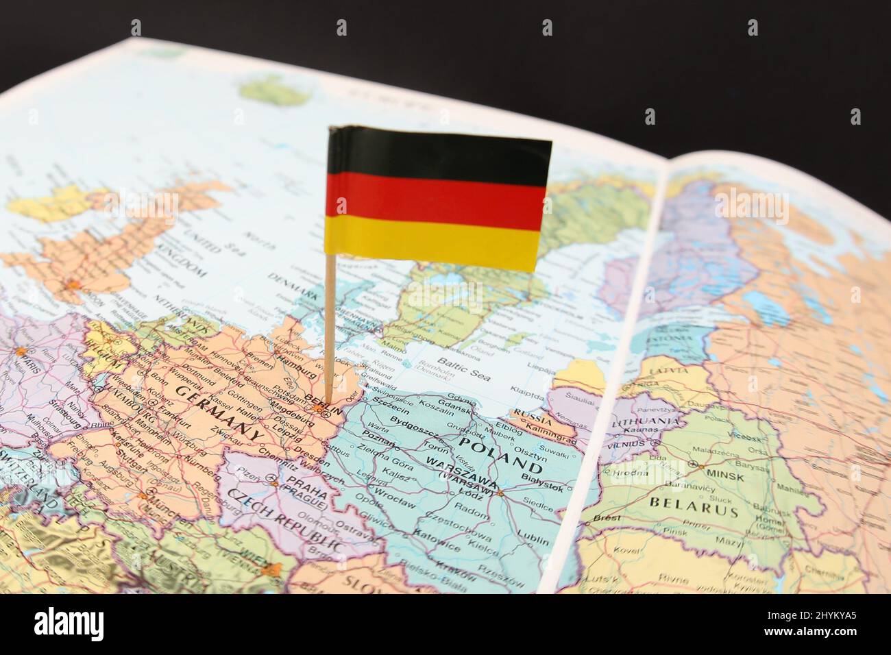 The German national flag sticking out of a close up image of a map or atlas focusing on Western Europe. The country of Germany with its neighbors. Stock Photo