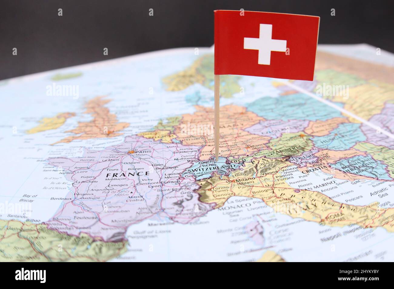 The Swiss national flag sticking out of a close up image of a colored map or atlas focussing on Europe. The country of Switzerland with its neighbours Stock Photo